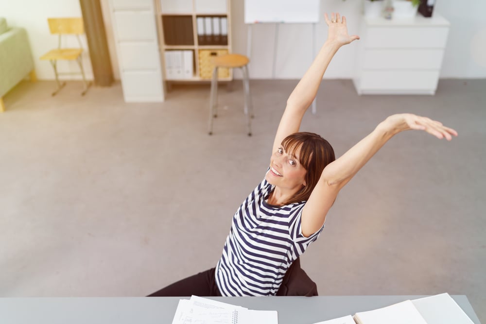 Happy Office Woman at her Table Stretching her Arms Up and Smiling at the Camera From a Higher Angle Point.