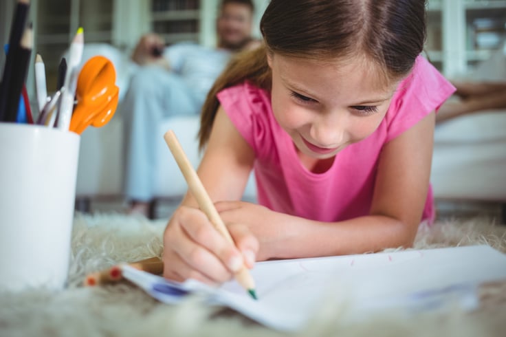 Smiling girl lying on the floor and drawing while parents sitting on sofa