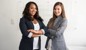 two smiling women in suits with crossed arms