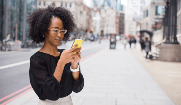 woman on street typing on yellow cell phone