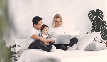 family looking at laptop and sitting on bed