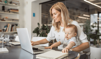 childcare educator holding baby while working on laptop