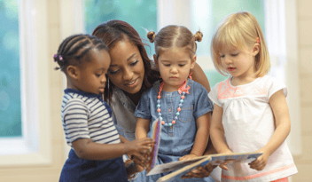 childcare center director helping young children read a book