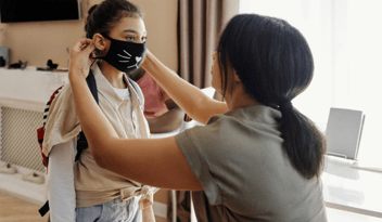 childcare provider helping young girl with covid-19 face mask